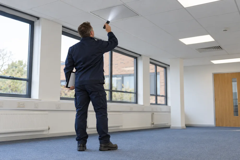 Surveyor inspecting a ceiling access point in an empty commercial office